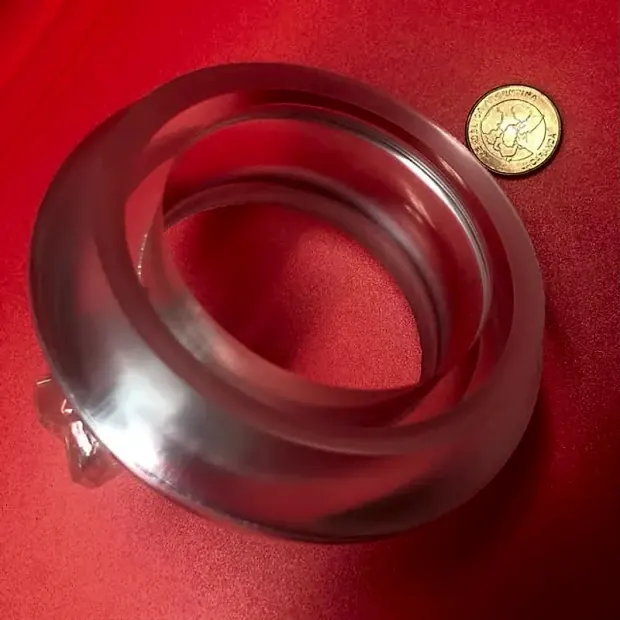 Anillo de plástico transparente sobre fondo rojo, junto a una moneda
