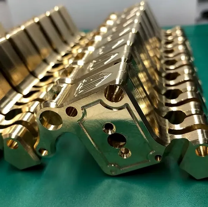 Pieza de latón con perforaciones y mecanizado de detalle sobre fondo verde